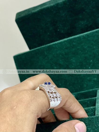 Silver ring with blue stones on a hand, against a green jewelry box background.