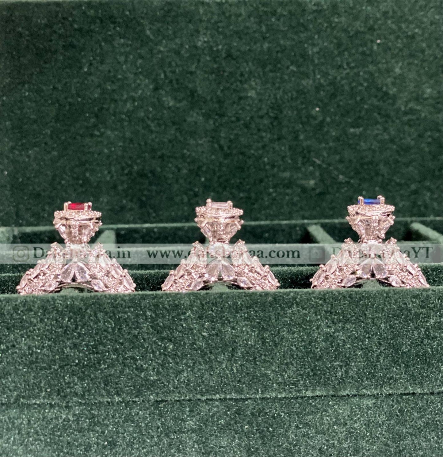 Three diamond earrings on a green cushion with a blurred background