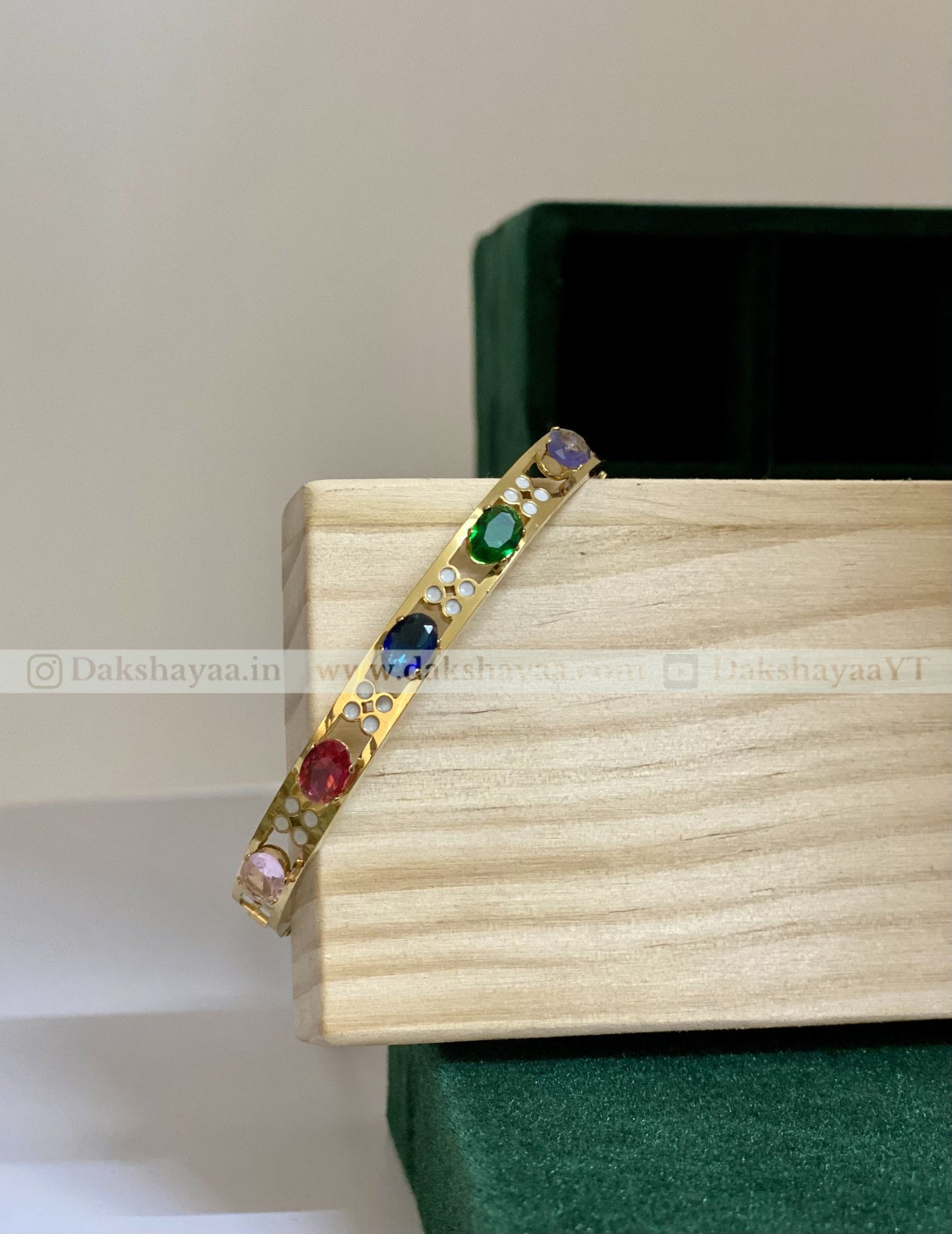 Gold bracelet with colorful gemstones on a wooden box
