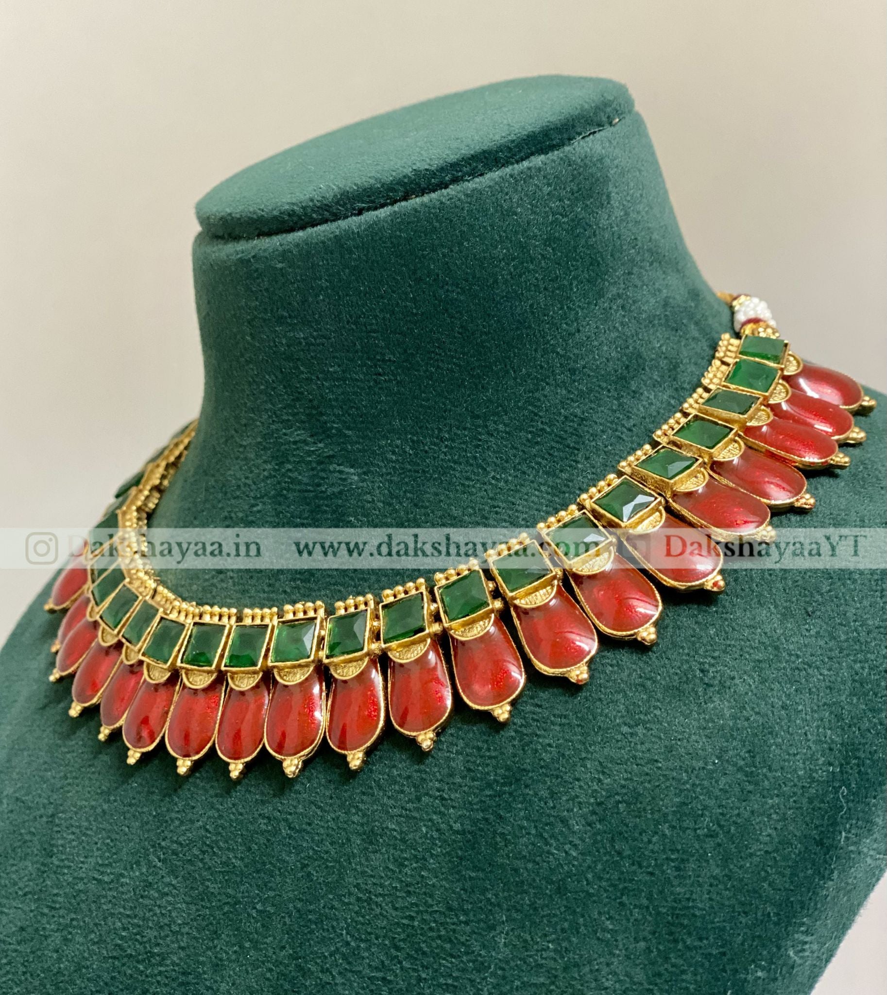 Ornate necklace with red and green stones on a green velvet stand