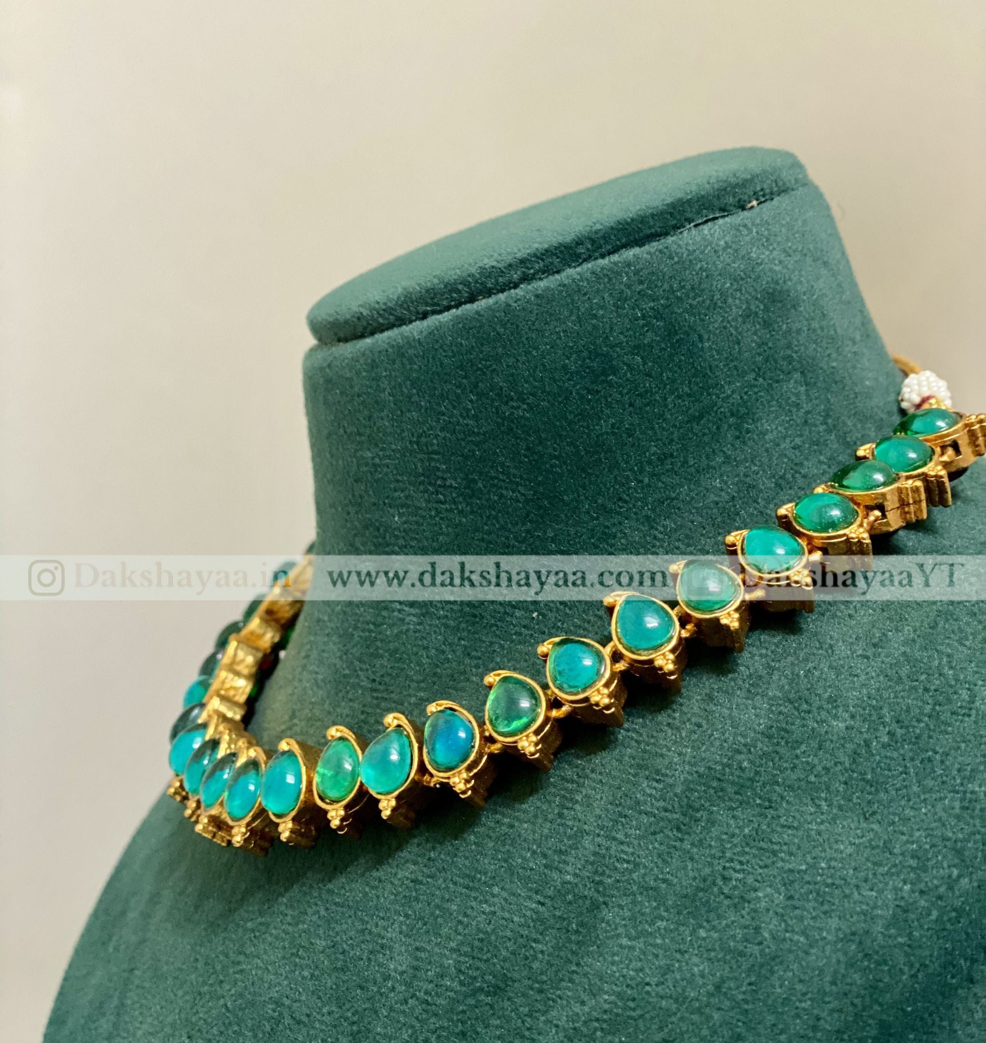 Gold necklace with green gemstones on a green velvet stand