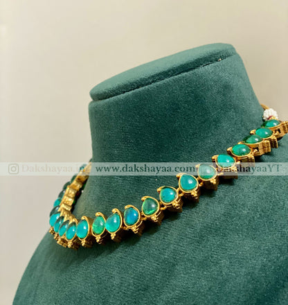 Gold necklace with green gemstones on a green velvet stand