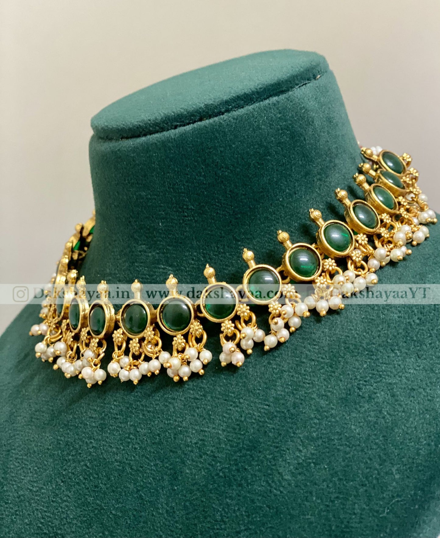 Ornate necklace with green stones and gold accents on a green velvet stand.