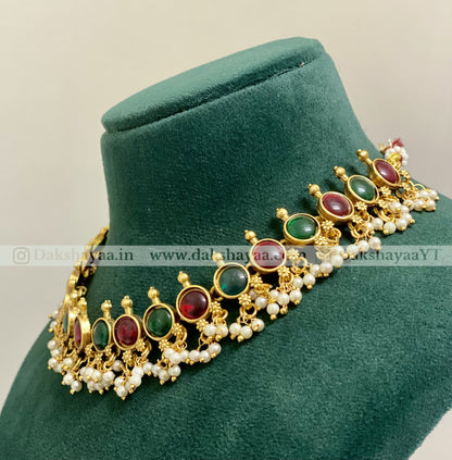 Gold necklace with red and green gemstones on a green velvet stand