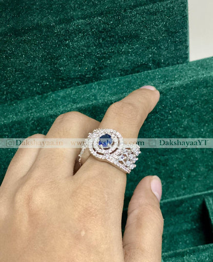 Silver ring with a blue gemstone on a finger against a green background