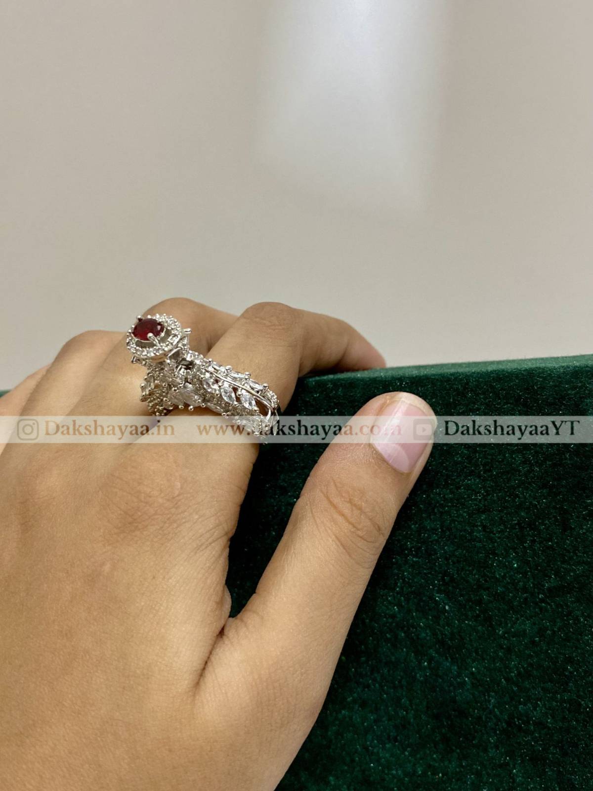 Hand wearing a silver ring with a red gemstone on a green surface