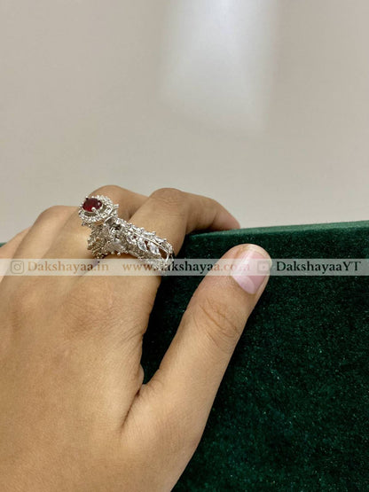 Hand wearing a silver ring with a red gemstone on a green surface