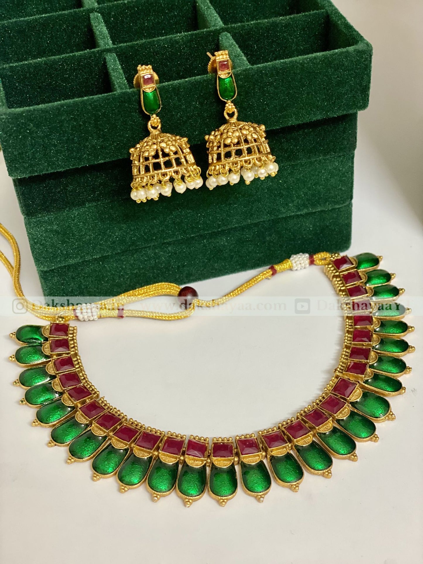 Gold necklace with green and red stones and matching earrings on a green velvet box.