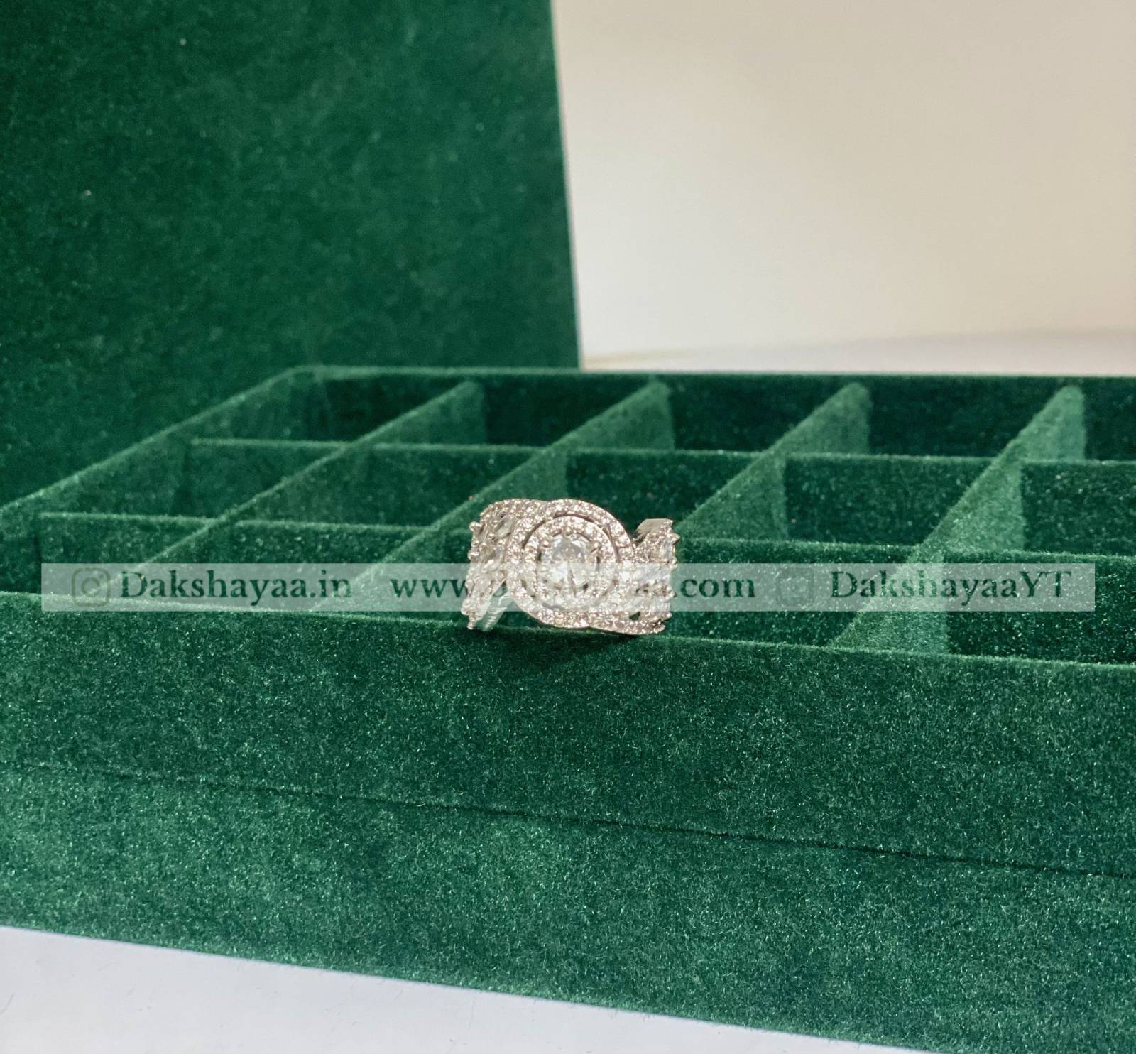 Silver ring on a green jewelry box with visible branding.